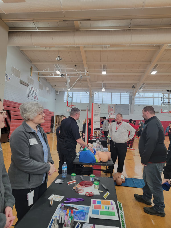 Michele G. Harms, program director from UPMC CHQ Medical Laboratory Science Program, and her colleague tabling in the gym and promoting health care education. Catt. Co. EMS seen in the background.